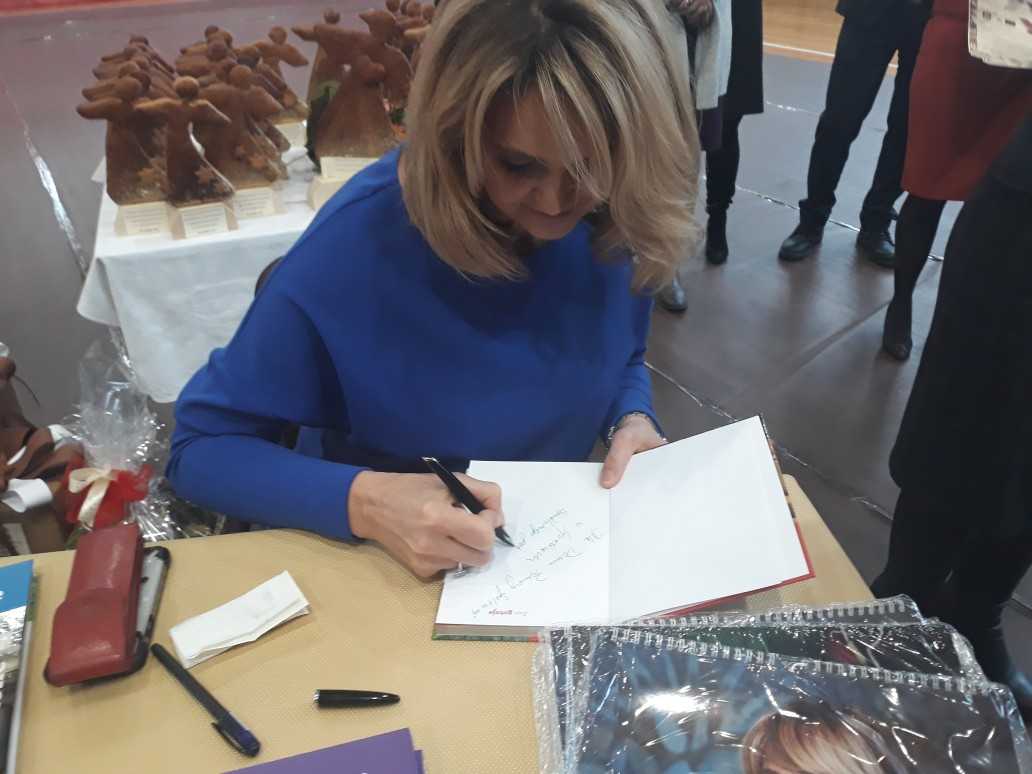 Ewa Wachowicz podpisuje książkę kucharską - nagrodę dla DPS