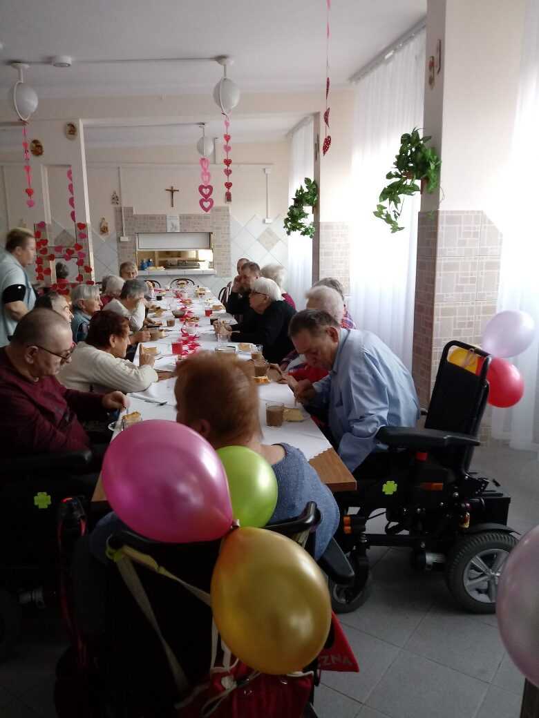 mieszkańcy podczas zabawy walentynkowej siedzą przy stołach i jedzą przygotowany poczęstunek