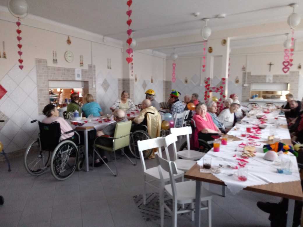 mieszkańcy podczas zabawy walentynkowej siedzą przy stołach i rozmawiają