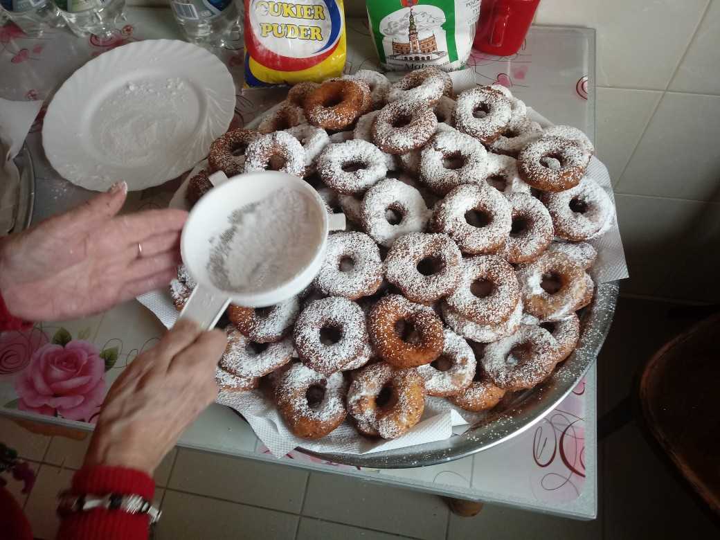 mieszkanka DPS posypuje cukrem pudrem oponki z serem