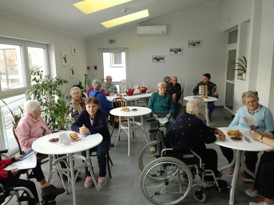 mieszkańcy siedzą przy stolikach, częstują się przygotowanymi przekąskami i śpiewają kolędy