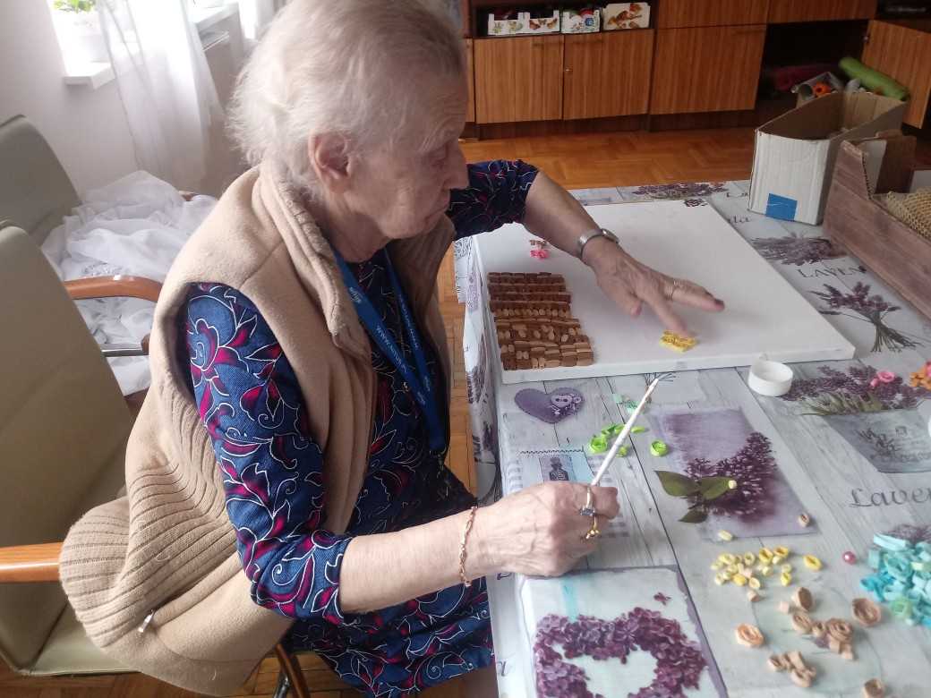 mieszkanka DPS siedzi przy stole i wykleja obrazek