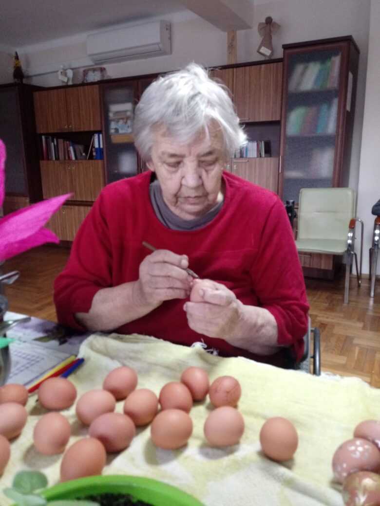 mieszkanka DPS siedzi na wózku inwalidzkim i rysuje pisakiem wzory na jajku