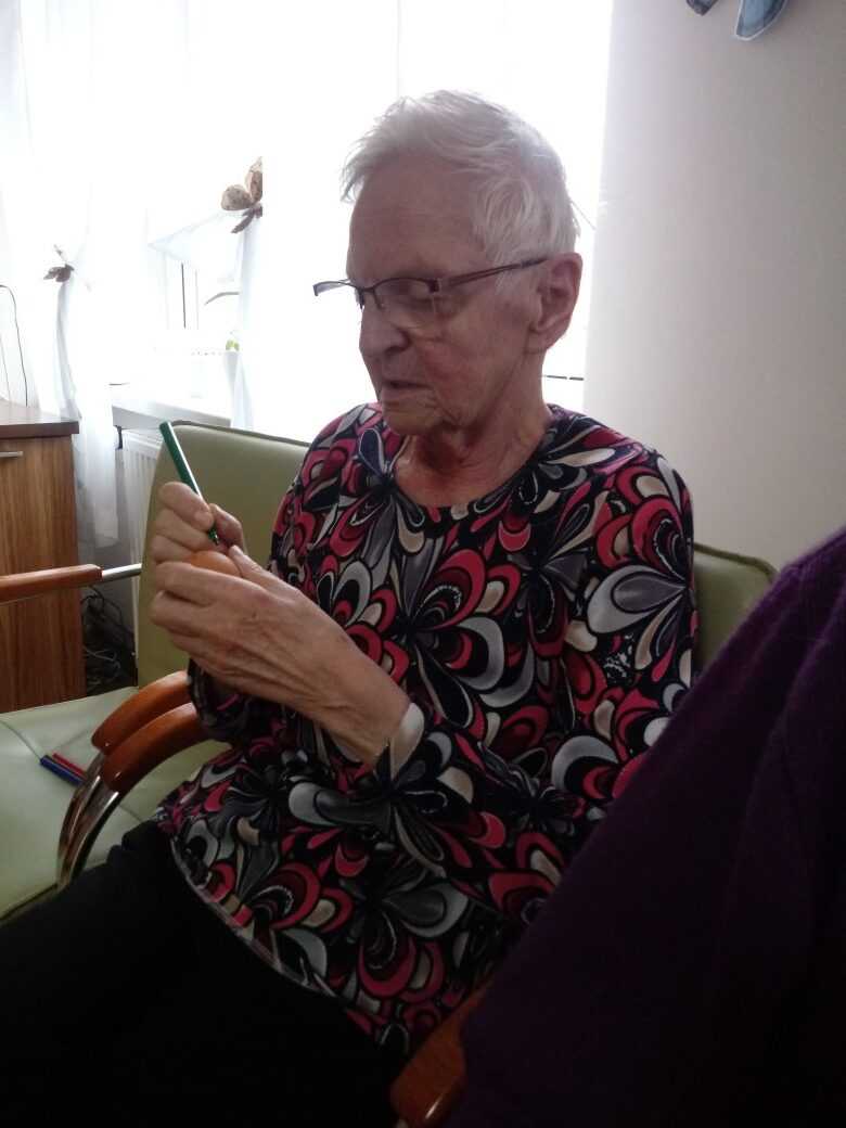 mieszkanka DPS siedzi na fotelu i maluje pisakiem wzory na jajku