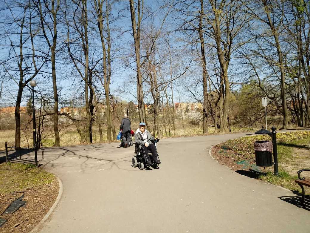 mieszkaniec DPS na wózku inwalidzkim pozuje do zdjęcia w scenerii parku miejskiego