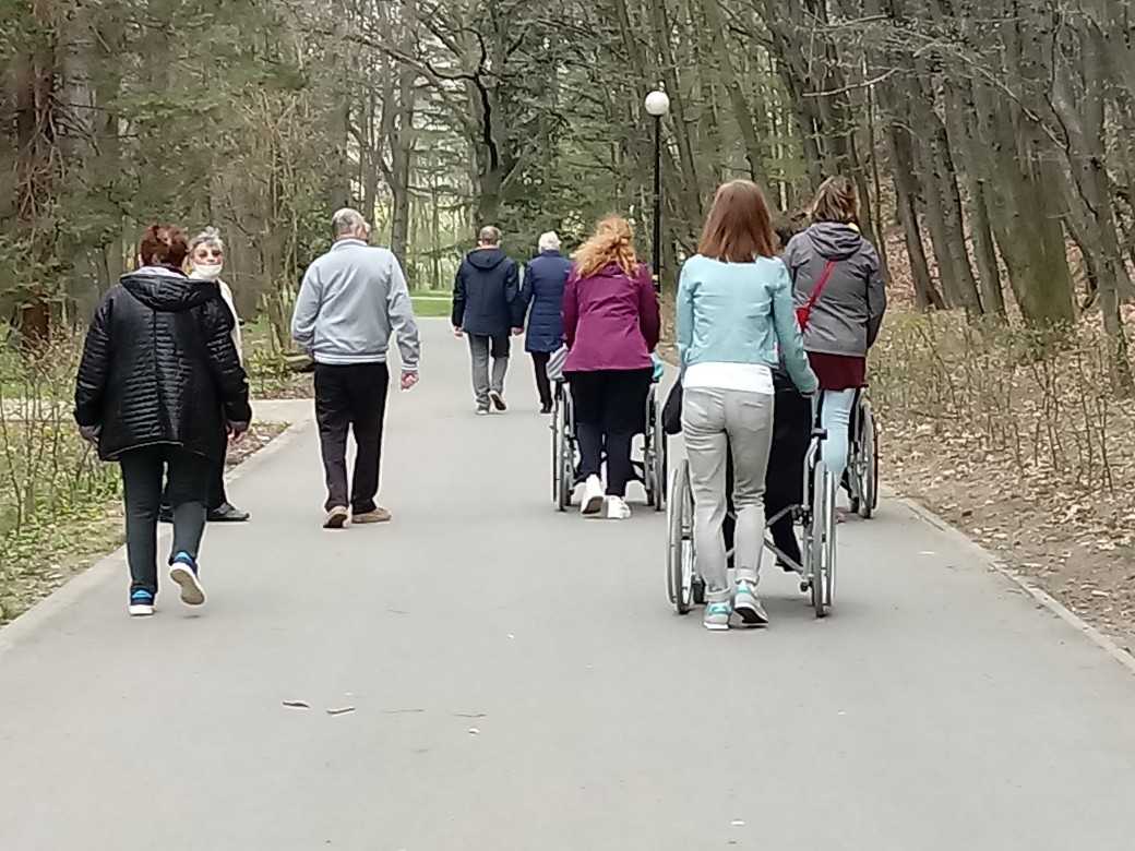 mieszkańcy i pracownicy DPS spacerują alejką w parku miejskim