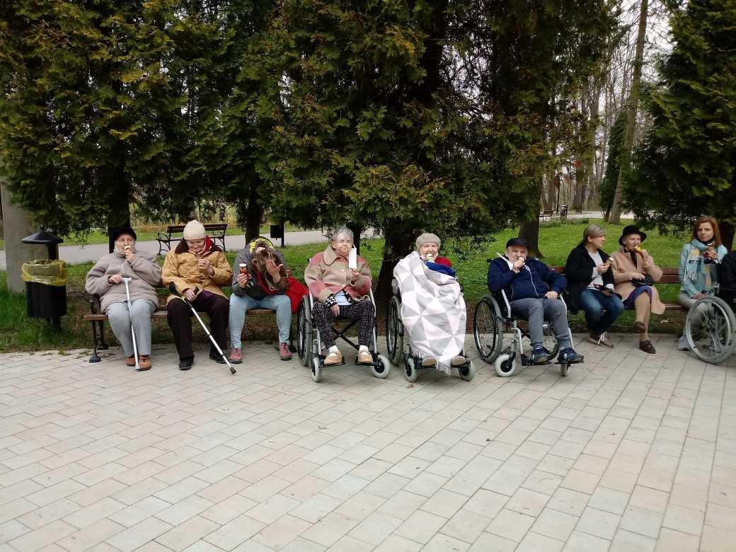 mieszkańcy DPS odpoczywają na ławkach w parku