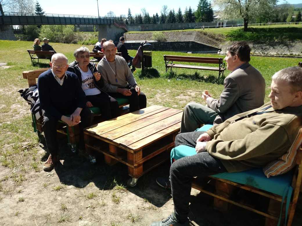 mieszkańcy DPS siedzą przy stoliku w parkowej kawiarence nad rzeką i rozmawiają