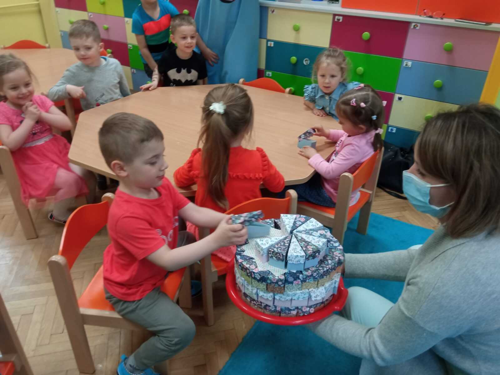 pracownik DPS odwiedza dzieci z sąsiedniego przedszkola i częstuje je cukierkami ukrytymi w papierowych pudełeczkach ułożonych w kształcie tortu