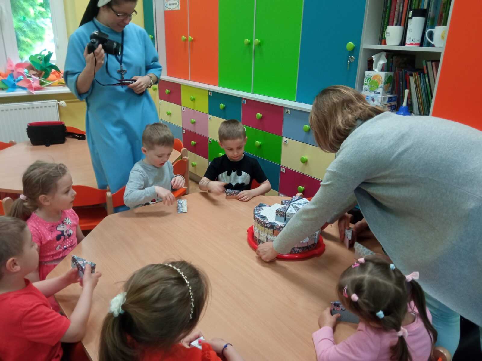 Pracownik DPS częstuje dzieci słodkościami z okazji dnia dziecka.