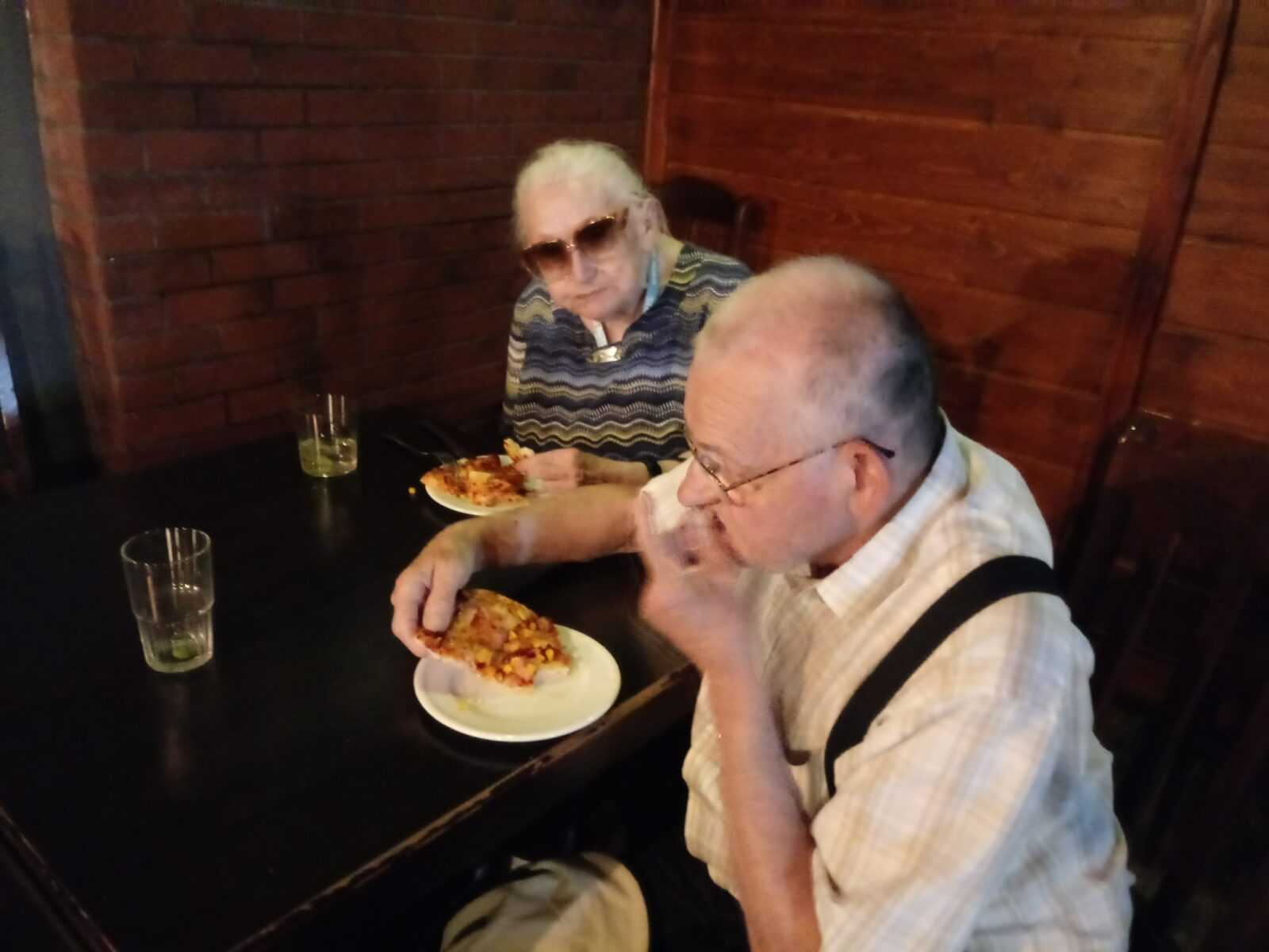 mieszkaniec i mieszkanka DPS siedzą przy stole i jedzą domową pizzę