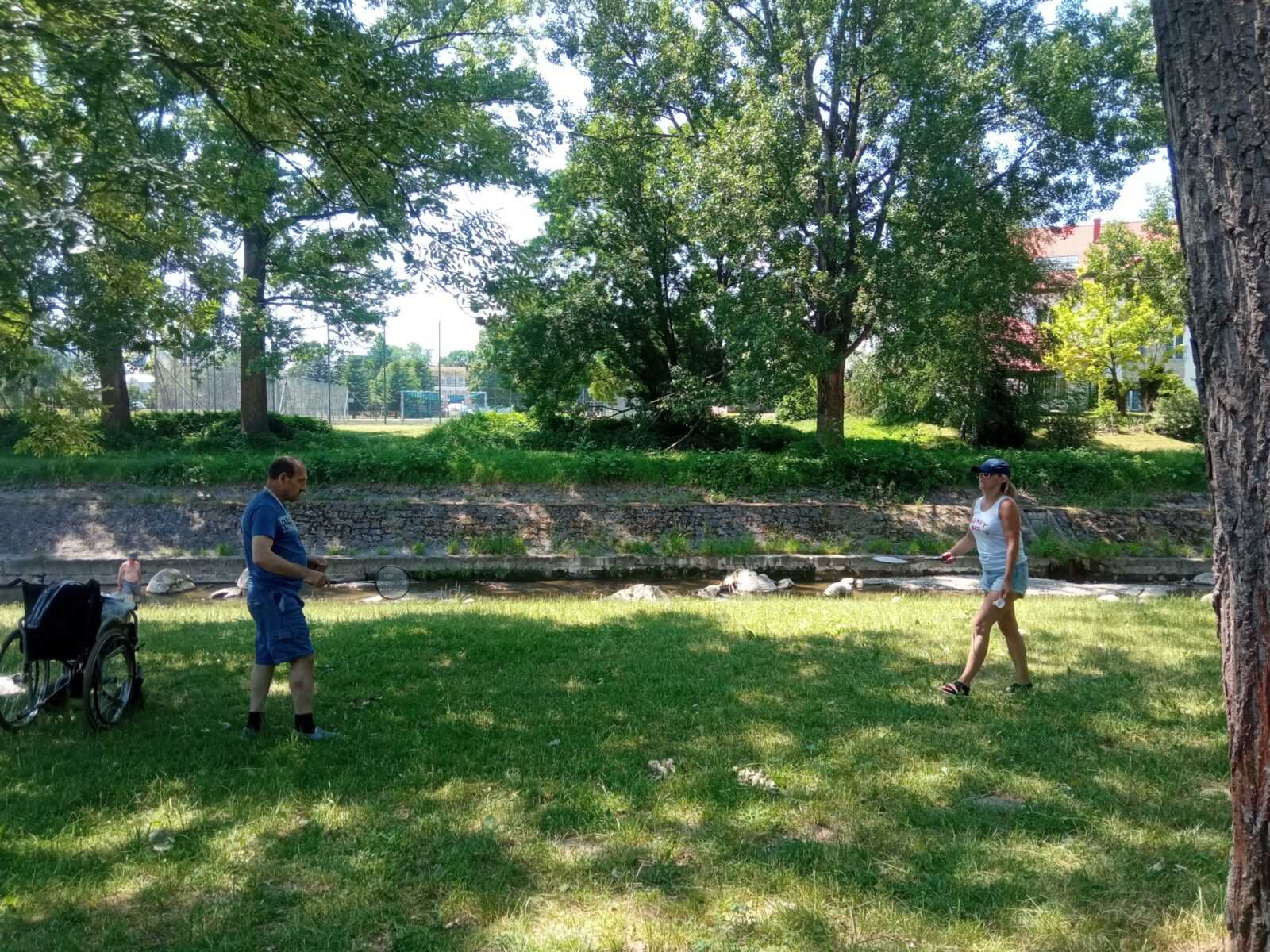 w cieniu drzew parkowych na trawie pracownica DPS gra w badmintona z mieszkańcem