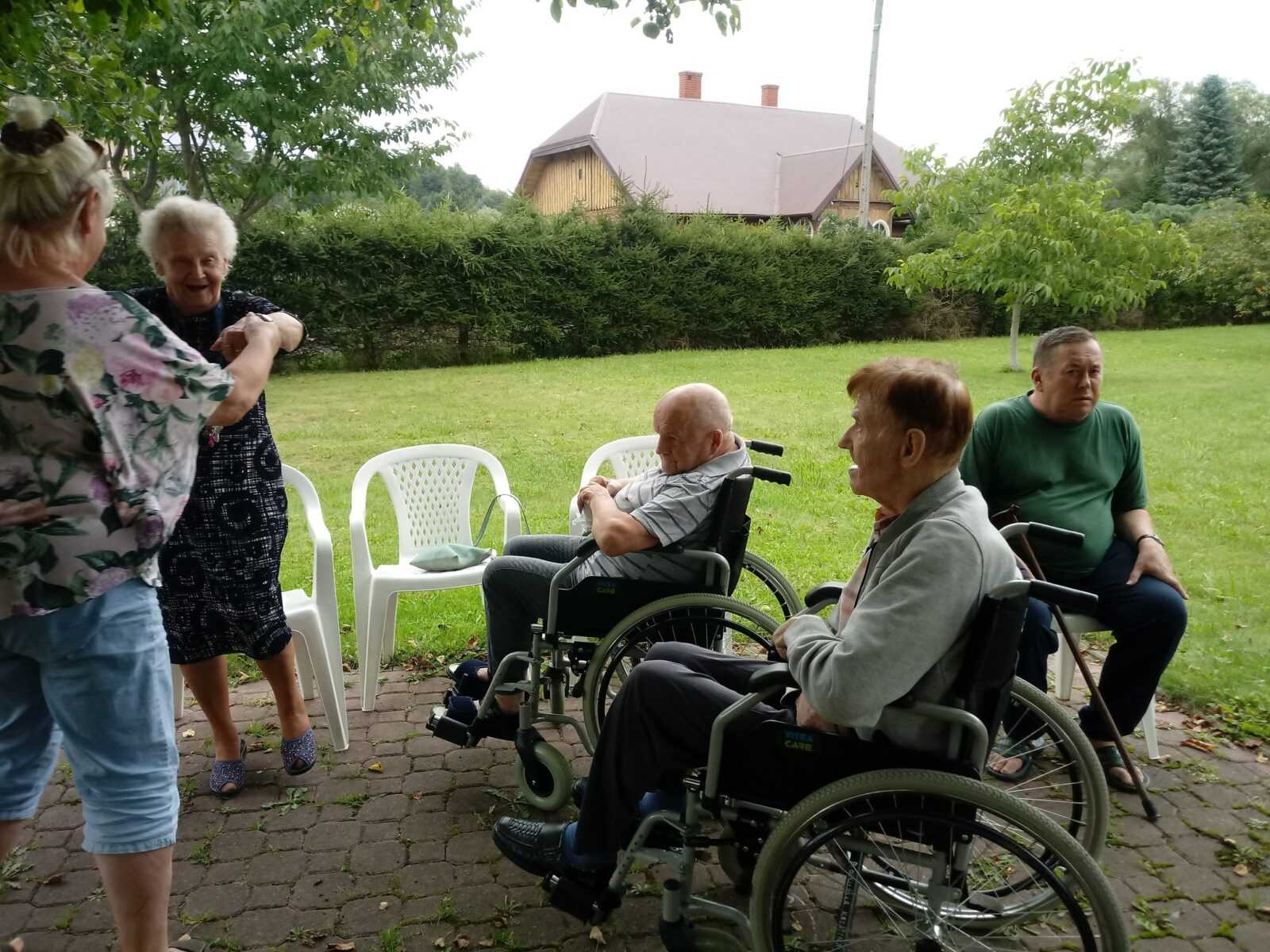 mieszkańcy DPS siedzą w ogrodzie, obserwują tańczących