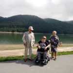 dwie starsze panie i starszy pan pozują do zdjęcia na tle jeziora i gór