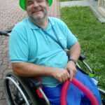 niepełnosprawny mężczyzna w zielonym kapeluszu i balonem w ręce uśmiecha się do aparatu